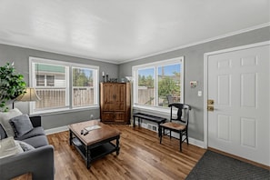 A room with a wooden floor, a gray sofa, a coffee table, a wooden cabinet, and a bench.
