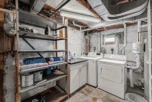 A laundry room with a washing machine, a sink, and shelves with cleaning supplies. - Cozy Rapid City Home w/ Hot Tub & Patio (Rapid City)