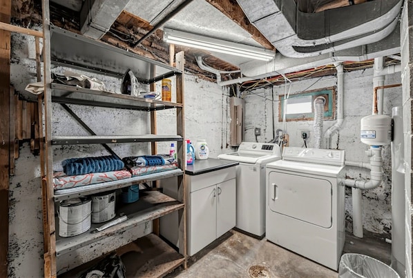 A laundry room with a washing machine, a sink, and shelves with cleaning supplies.