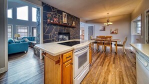 Una cocina moderna con protector contra salpicaduras de piedra, una estufa empotrada y un comedor con sillas y mesa de madera.