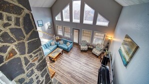 Amplia sala de estar tipo loft con una pared de acento de piedra, un sofá seccional azul, un sillón estampado y un ventanal de múltiples paneles.
