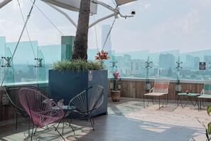 Eine Dachterrasse mit Sitzgelegenheiten, Topfpflanzen und Blick auf die Stadt.