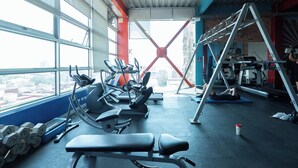 A gym with exercise equipment, a window with a city view, and a red structural element. - The Green Escape Suite (Mexico City)