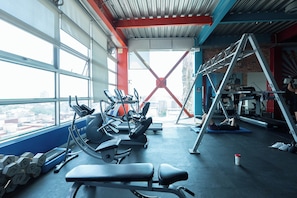 A gym with exercise equipment, a window with a city view, and a red structural element. - The Green Escape Suite (Mexico City)