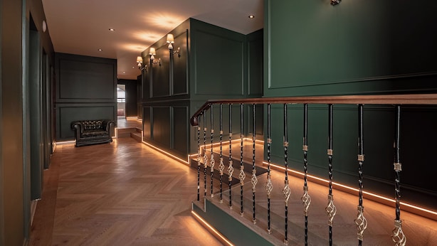 A staircase with a wooden handrail and black balusters, leading to a landing with a bench and wall sconces. - The Green Escape Suite (Mexico City)