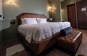 A neatly made bed with a headboard, a bedside lamp, and a brown leather ottoman. - The Green Escape Suite (Mexico City)