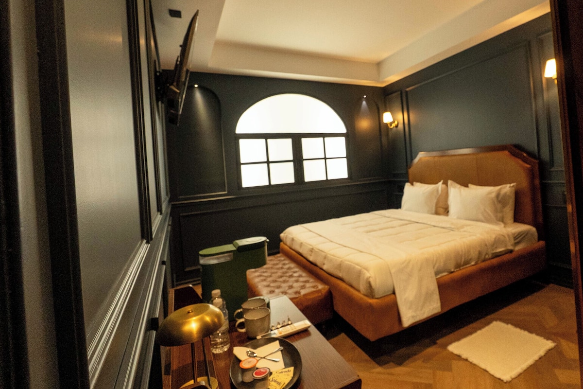 Ein Schlafzimmer mit einem Bett, einem Nachttisch, einer Lampe, einem Fenster und einem an der Wand befestigten Fernseher.