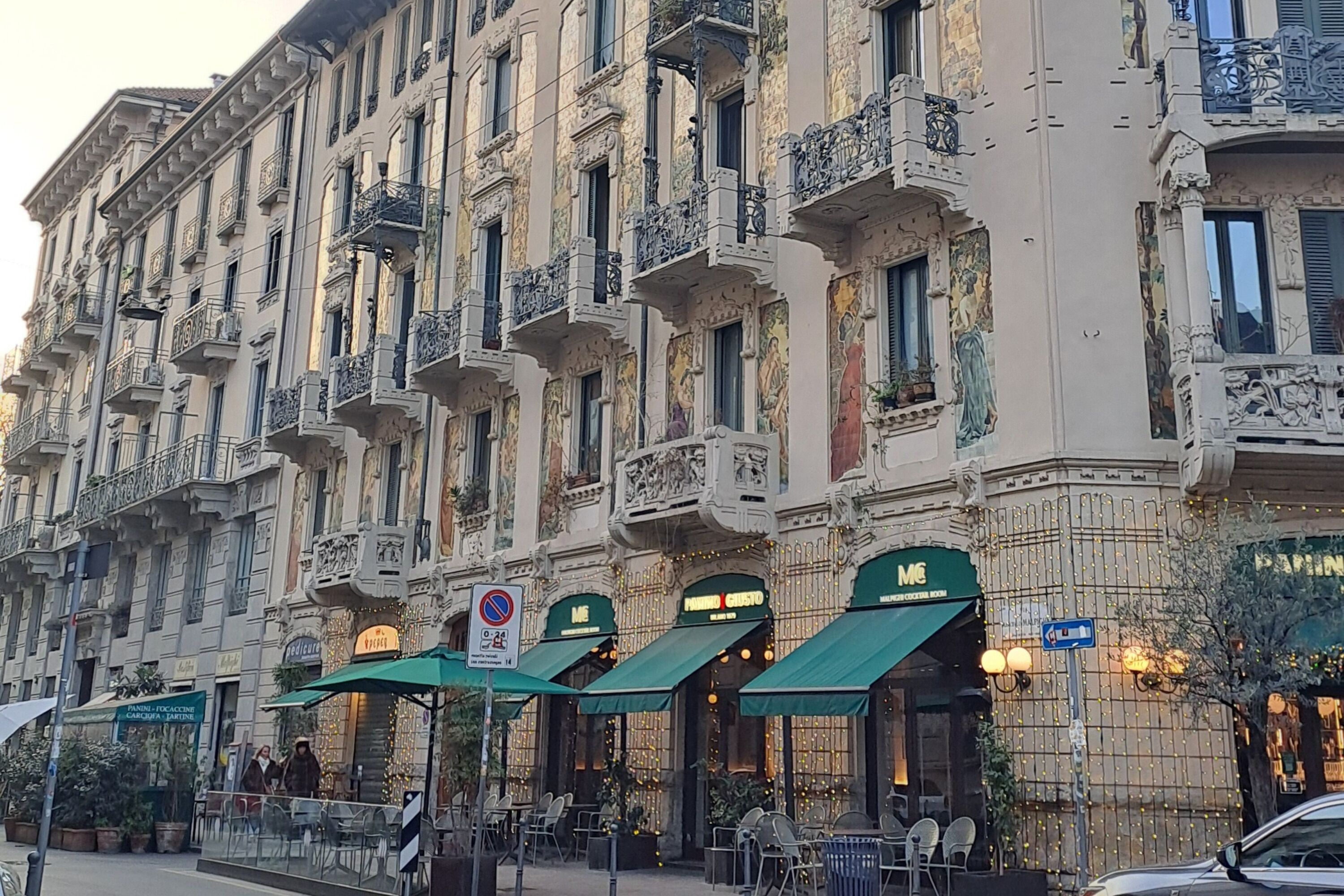 Ein historisches Gebäude mit aufwendigen Balkonen und einem Restaurant namens "Pizzeria Gusto" mit Außenplätzen.
