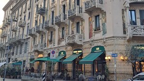 Ein historisches Gebäude mit aufwendigen Balkonen und einem Restaurant namens "Pizzeria Gusto" mit Außenplätzen.
