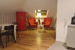 Ein kompakter Wohnraum mit Essbereich, einem roten Kühlschrank, zwei roten Stühlen, einem kleinen Tisch mit Lampe und einem Fernseher auf einem Schrank.