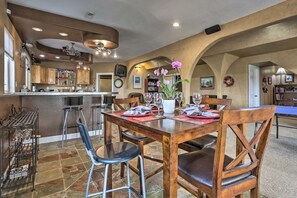Ein Essbereich mit einem Holztisch, gedeckt für vier Personen, umgeben von Stühlen. Im Hintergrund ist eine Küche mit einer Bar erkennbar.
