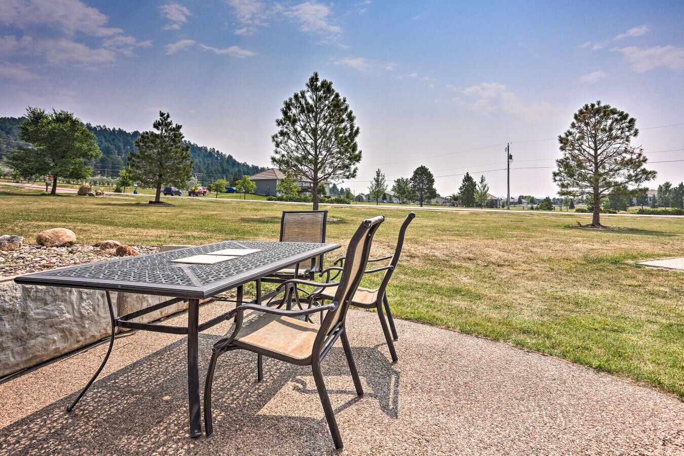 Un espace extérieur aménagé avec une table et des chaises en métal, entouré d’un champ herbeux et d’arbres.