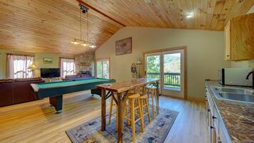A cozy room with a pool table, a bar area, and a kitchen.