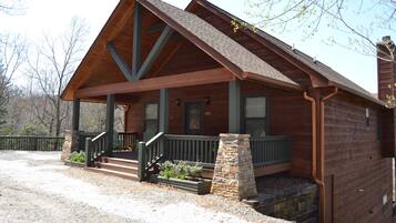 A wooden cabin with a porch, stone steps, and a chimney.