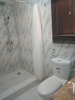 A bathroom with a shower, toilet, and marble walls. - Duchess Hotel and Spa (Abuja)