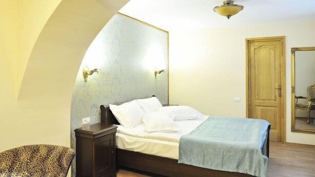 A bedroom with a bed, a nightstand, a chair, and a wooden door. - Safrano (Brasov)