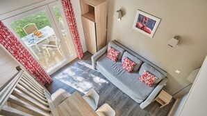 Een moderne woonkamer met een bank, stoelen, een eettafel en uitzicht op de tuin door grote ramen.
