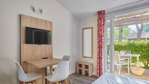 Een moderne kamer met een bed, een bureau met twee stoelen, een aan de muur bevestigde televisie en een groot raam met uitzicht op groen en een traditioneel gebouw.
