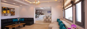 A modern living room with a black sofa, teal cushions, a wooden coffee table, and a large abstract painting on the wall. - Tropicana Hotel (Mykonos)