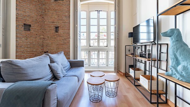 Ein modernes Wohnzimmer mit Backsteinwand, grauem Sofa, Fernseher und einer dekorativen Hundestatue.