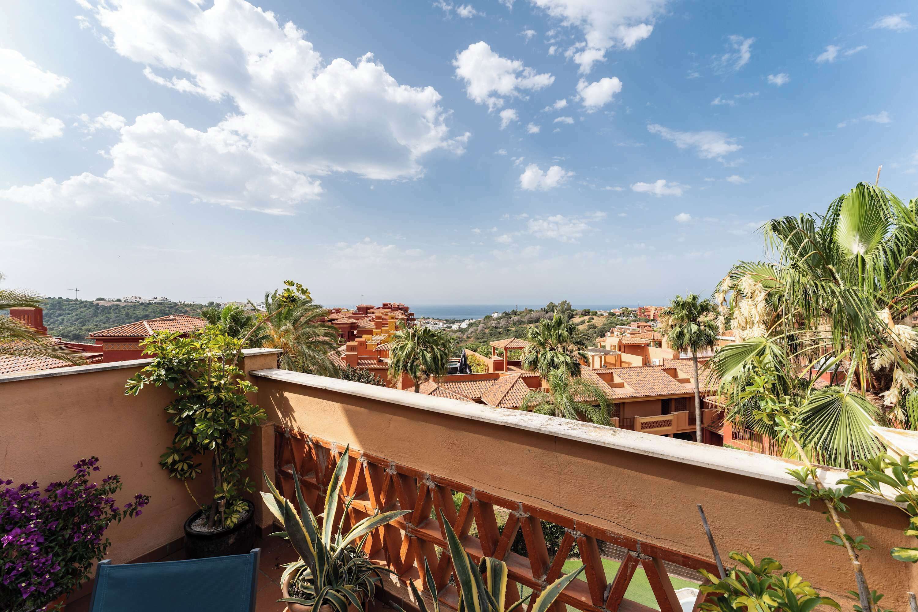 A balcony with a view of a coastal town, palm trees, and a clear sky.