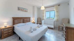 Un dormitorio con una cama grande, mesitas de noche, un escritorio, una silla, un radiador y una ventana con cortinas.