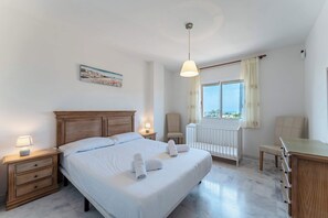 A bedroom with a large bed, bedside tables, a desk, a chair, a radiator, and a window with curtains. - SR Penthouse with sea views (Marbella)