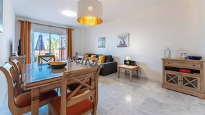 Una sala de estar moderna con comedor, que incluye una mesa de vidrio, sillas de madera, un sofá y una lámpara colgante.