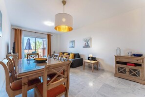 A modern living room with a dining area, featuring a glass-top table, wooden chairs, a sofa, and a hanging light fixture. - SR Penthouse with sea views (Marbella)