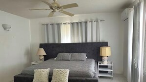 Una camera da letto con un letto, due comodini con lampade, una ventola a soffitto e una finestra con tende.