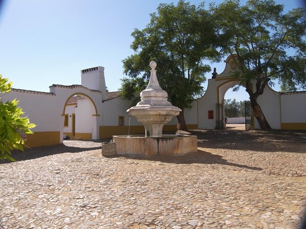 A courtyard with a stone fountain, white walls with yellow trim, and an archway. - Monte Da Amoreira (Elvas)