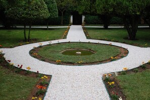 A formal garden with a central circular water feature, surrounded by a gravel path and bordered by flower beds. - Monte Da Amoreira (Elvas)