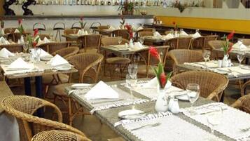 Restaurante com mobiliário de vime, mesas bem arrumadas com guardanapos brancos e um bar ao fundo.