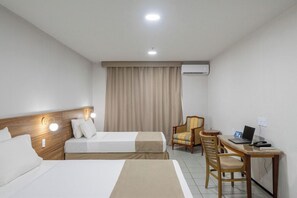 A hotel room with two beds, a desk with a laptop, a chair, and a curtain.