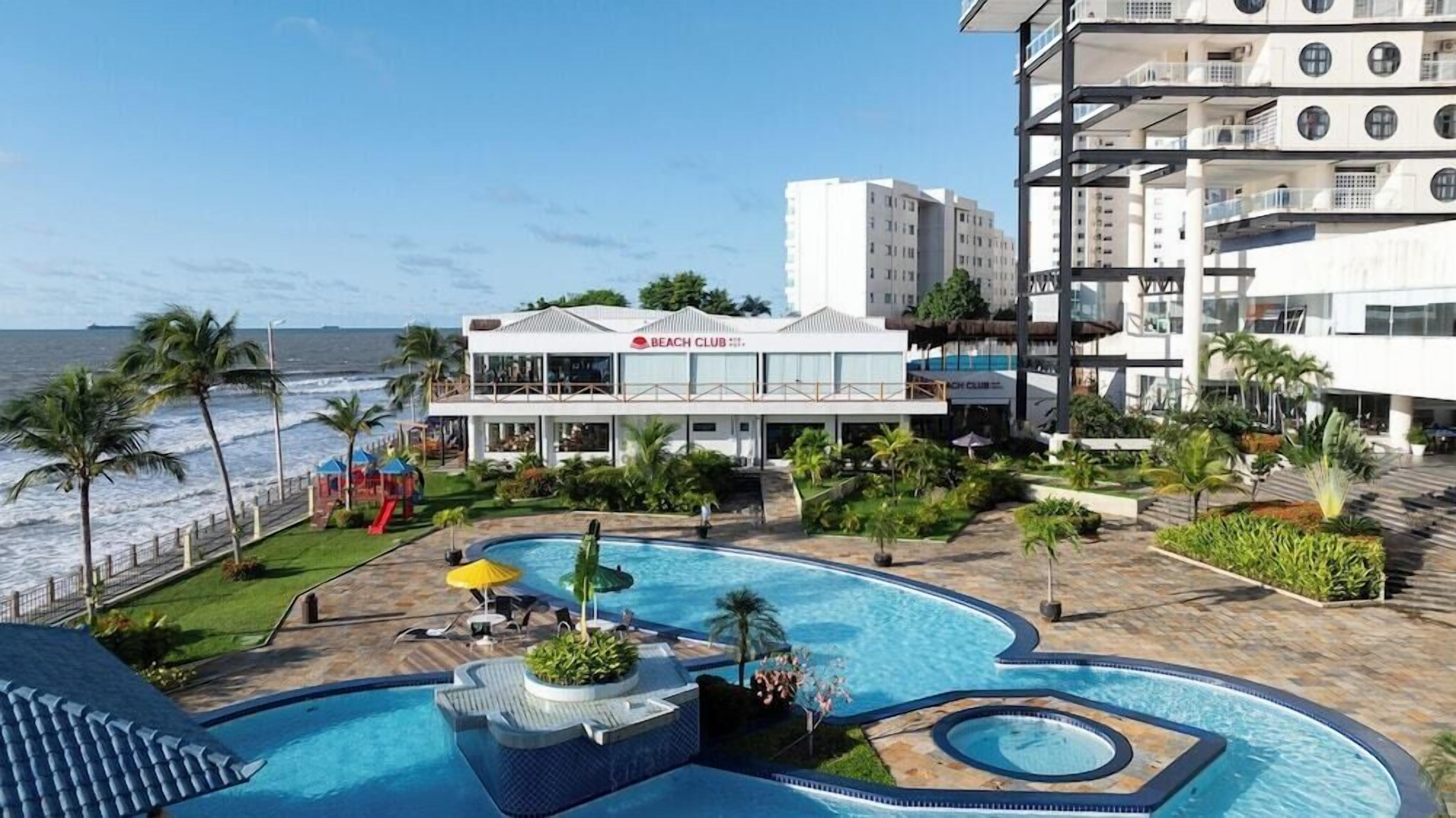 A beachfront hotel with a pool, palm trees, and a beach club.