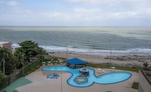 Een zwembad met een blauw ontwerp, een strand en uitzicht op de oceaan.