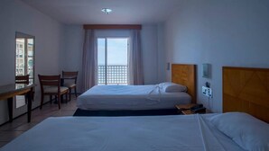 Habitació d'hotel amb dos llits, una taula, cadires i vista al mar per la finestra.