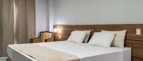 A hotel room with a large bed, a wooden headboard, a bedside table, and a chair.