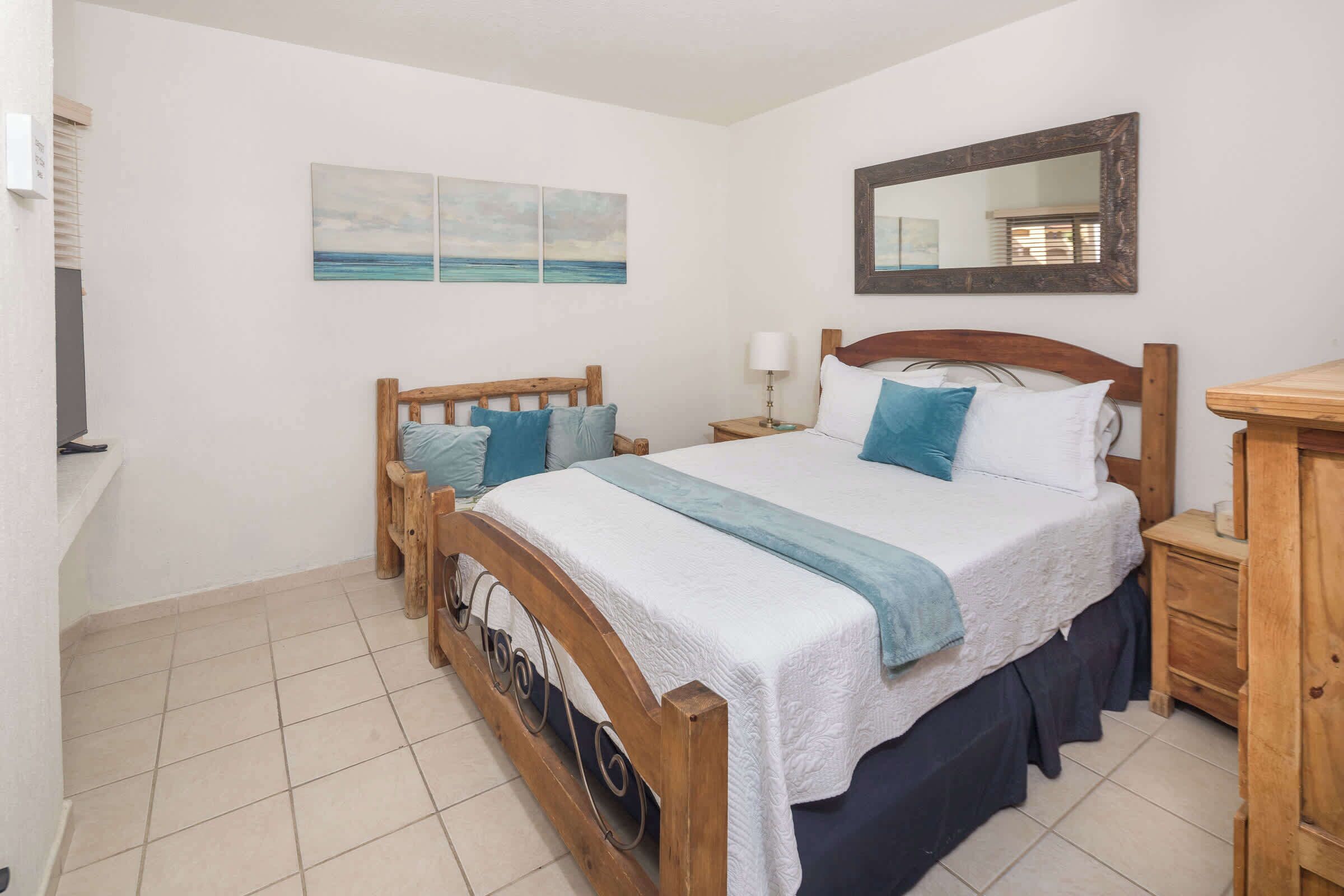 A bedroom with a wooden bed, a nightstand, a mirror, and artwork on the wall.