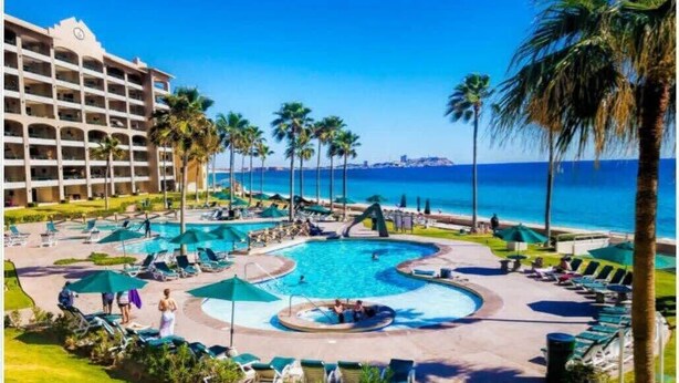 A hotel with a large pool area, palm trees, and a view of the ocean. - Oceanfront Sunsets at Sonoran Spa E305 (Puerto Peñasco)