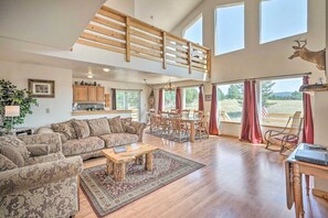 A spacious living room with a high ceiling, wooden staircase, and large windows. - Rocky Mtn Cabin w Views, Deck & Game Room (Florissant)