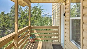 Een houten terras met een balustrade, een bloempot en uitzicht op bomen en bergen.