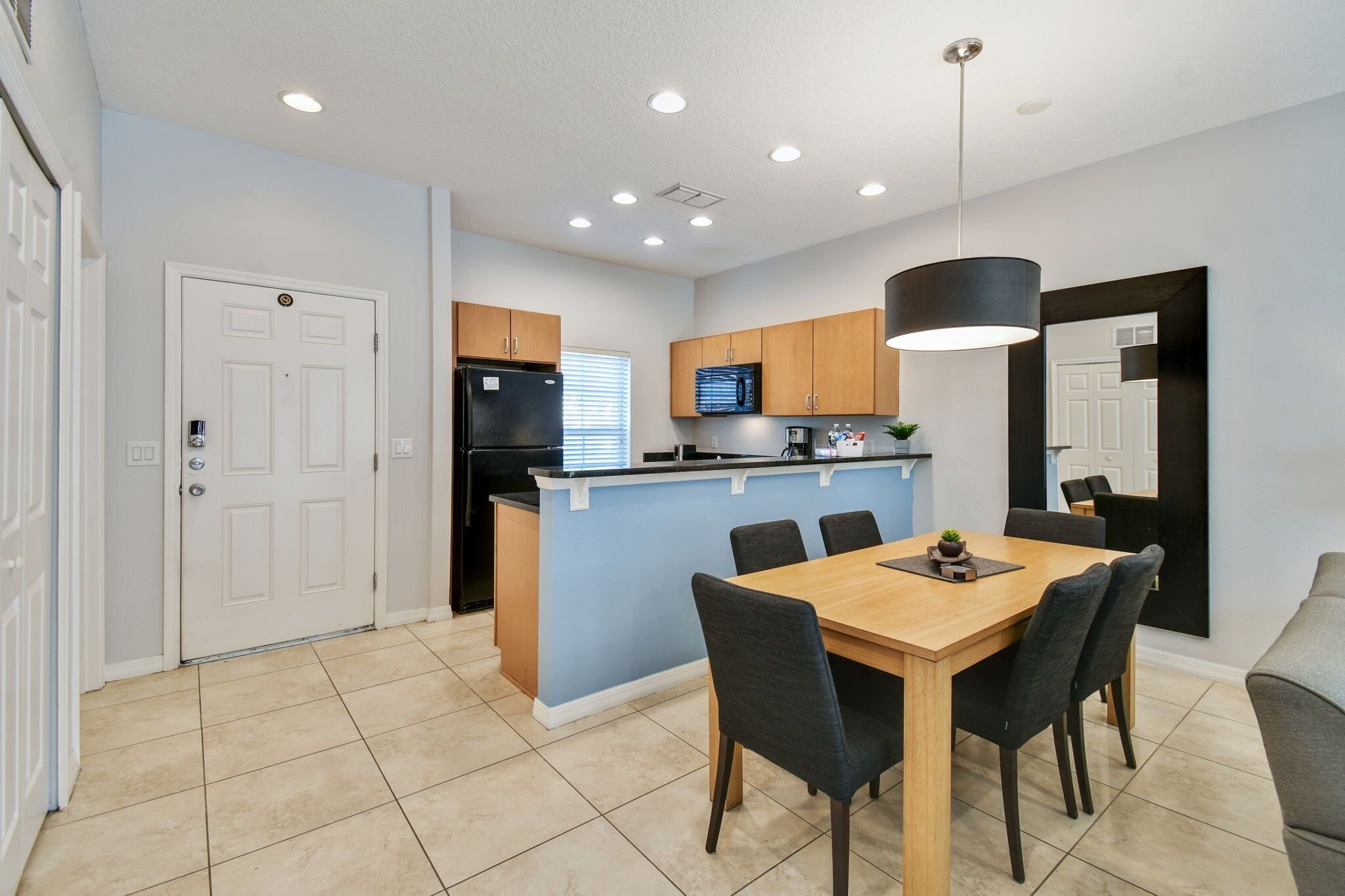 Una cocina moderna con una isla central, un área de comedor con una mesa y sillas de madera, y un espejo grande en la pared.