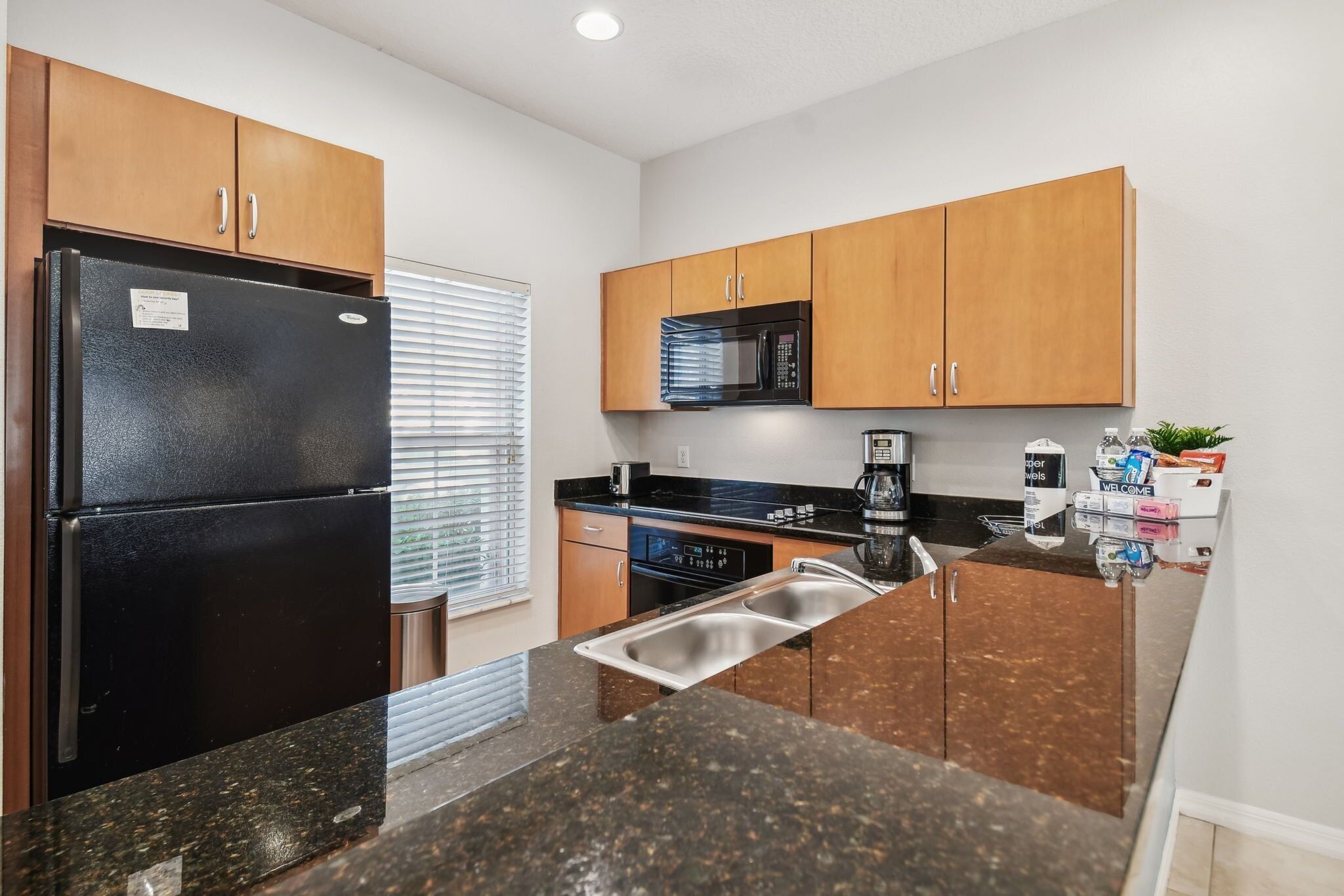 A kitchen with wooden cabinets, a black refrigerator, a microwave, a dishwasher, and a granite countertop.