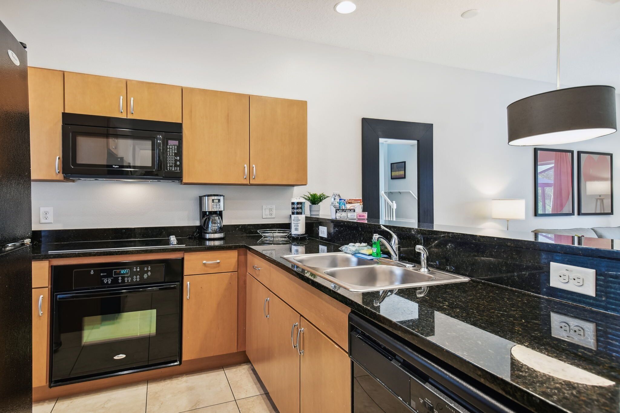 A modern kitchen with wooden cabinets, a black microwave, a built-in oven, a sink, and a black countertop.