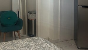 A compact room with a white door, a small trash bin, a teal chair, and a refrigerator. - Cozy Private Room 2 - Your Quiet Downtown Miami Getaway (Miami)
