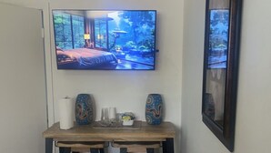 A dining area with a wooden table, two black chairs, a television mounted on the wall displaying a nature scene, and a framed picture on the wall. - Cozy Private Room 2 - Your Quiet Downtown Miami Getaway (Miami)