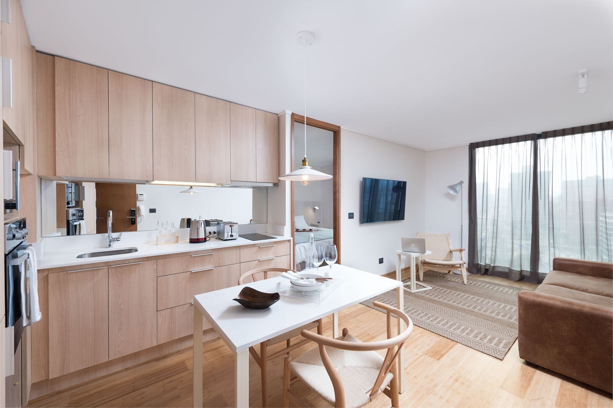A modern kitchen with wooden cabinets, a white countertop, and a dining area with a white table and chairs.