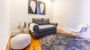 A modern living room with a grey sofa, a white rocking chair, a round grey rug, and a white knitted ottoman. - RM Guest House The Experience (Setubal)