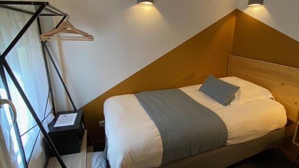 A bedroom with a bed, bedside tables, a hanging rack, and wall-mounted lights. - Hotel de la Marne (Lyon)